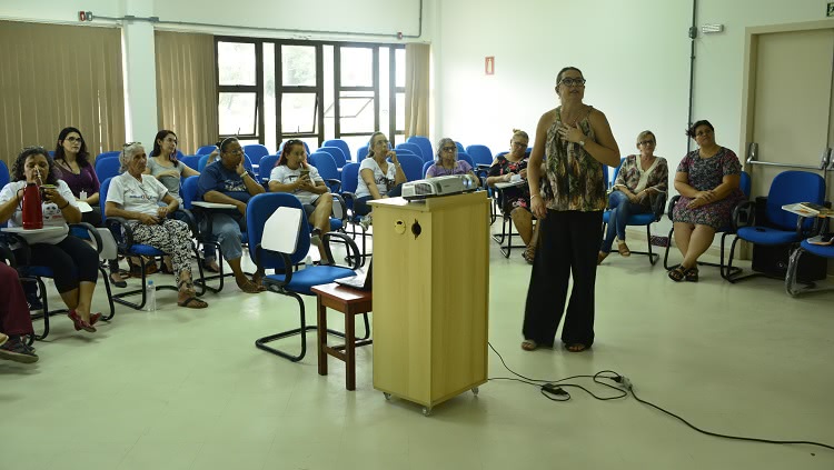 A assistente social da Proexc, Fernanda Fonseca, palestra em pé, em frente a um grupo de mulheres sentadas.
