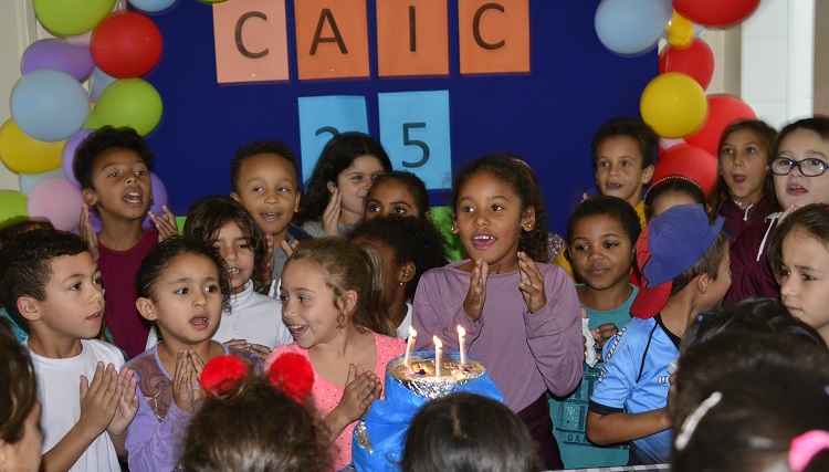A foto mostra crianças na volta do bolo de aniversário no refeitório do Caic.