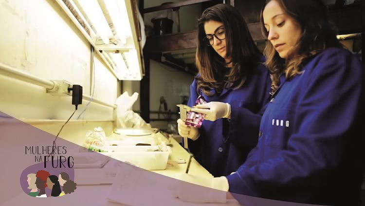 Em um laboratório duas jovens mulheres aparecem trabalhando. Uma delas é Ana Luzia. Ambas usam jalecos azuis em que consta a inscrição “Furg”. 