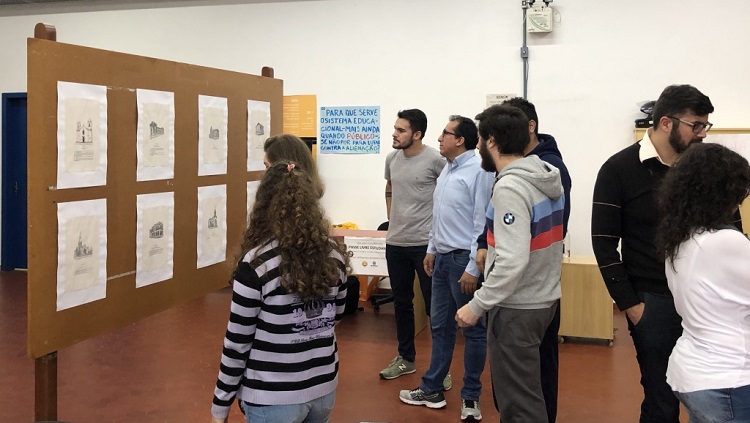 A foto mostra um grupo de pessoas virado para um painel onde estão expostos os desenhos do professor Antônio Valente.